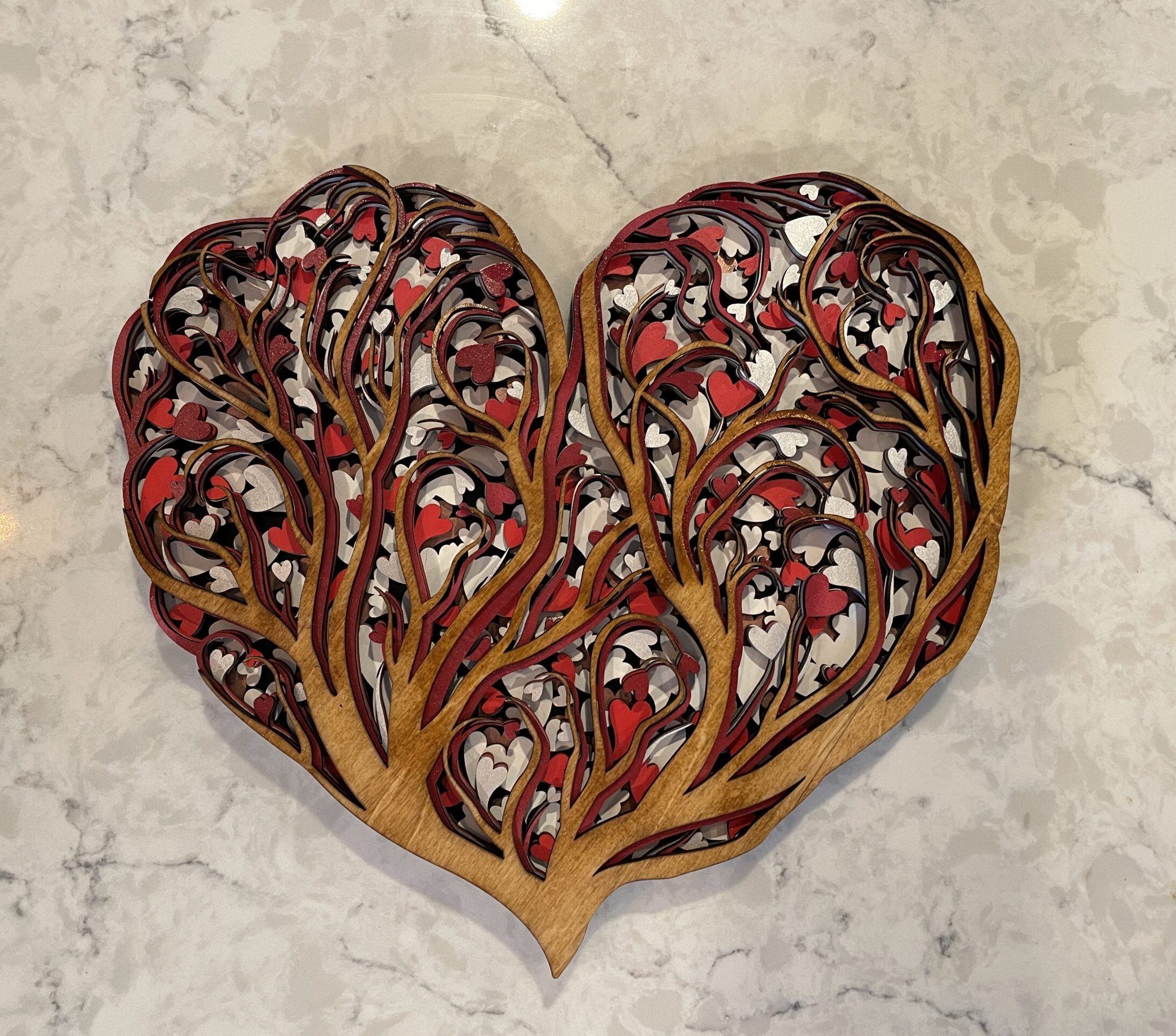 Handcrafted heart-shaped mandala with intricate tree branches and heart leaves. Stained wood front layer with shades of red, white, black, silver, maroon, and rose gold. Ideal for expressing love on Mother's Day or Valentine's.