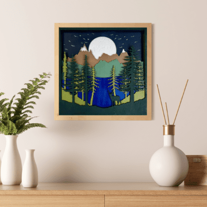 A physical wall art piece featuring a mountain mandala design, composed of seven stained basswood layers, each laser-cut to depict various natural elements. The artwork is 11.5 inches square and 0.75 inches thick, displaying scenes including the moon, birds, mountains, hills, a blue lake, trees, and a deer, all crafted with detailed wood grains to enhance its rustic aesthetic. by Encintias3D.com