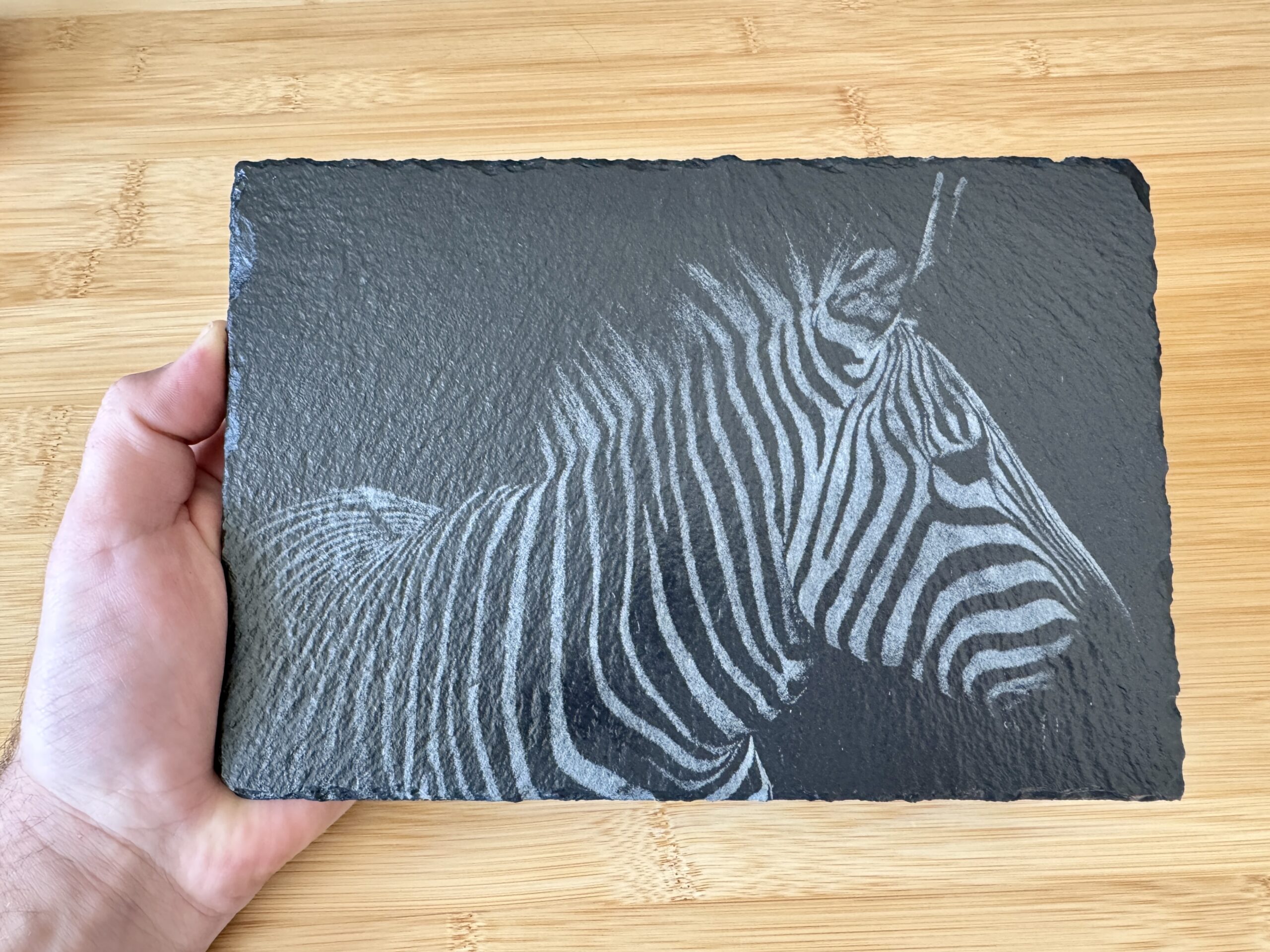 “High-contrast black and white image of a zebra with detailed stripes engraved onto a natural slate tile. The unique texture of the slate adds depth to the zebra’s distinct patterns, creating a striking, artistic effect. Perfect as a decorative piece or a custom gift from Encinitas3D.com, where technology meets nature-inspired design.”