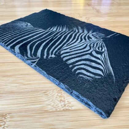 “High-contrast black and white image of a zebra with detailed stripes engraved onto a natural slate tile. The unique texture of the slate adds depth to the zebra’s distinct patterns, creating a striking, artistic effect. Perfect as a decorative piece or a custom gift from Encinitas3D.com, where technology meets nature-inspired design.”