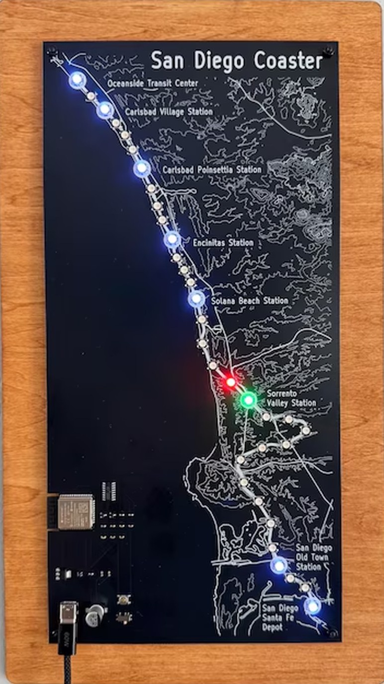 The sign on a wall: stations lit blue, a red northbound and a green southbound train passing near Sorrento Valley
